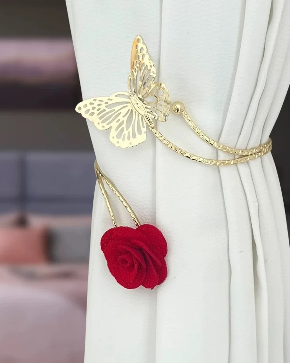 Gold-tone butterfly curtain tieback with fine curved chains and a suspended red fabric rose on an ivory curtain.