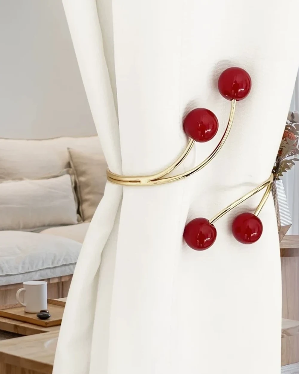 Glossy red spheres on curved gold-tone metallic curtain tiebacks around an ivory curtain.