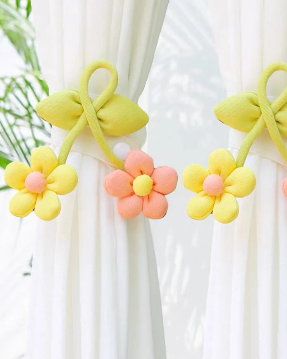 Yellow bows with hanging yellow and coral-pink fabric daisies decorating two white curtains.
