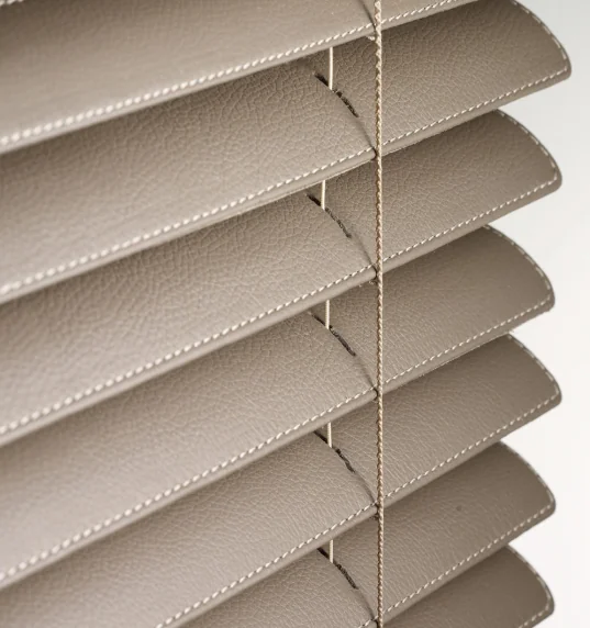 Close-up of beige pebbled, stitched horizontal Venetian slats and ladder cords.