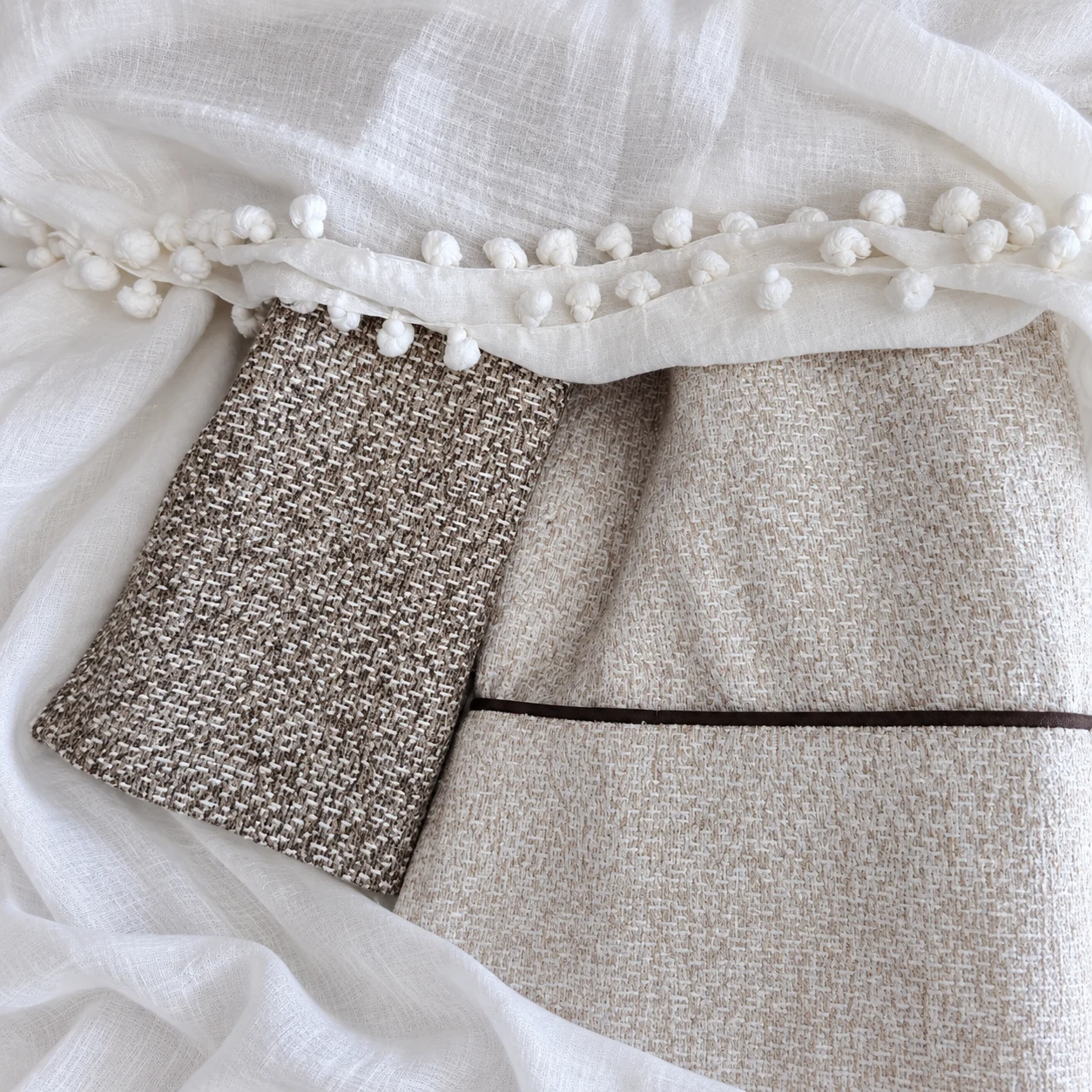 Neutral coordinating fabrics with narrow dark piping and small white pom-pom finishing.
