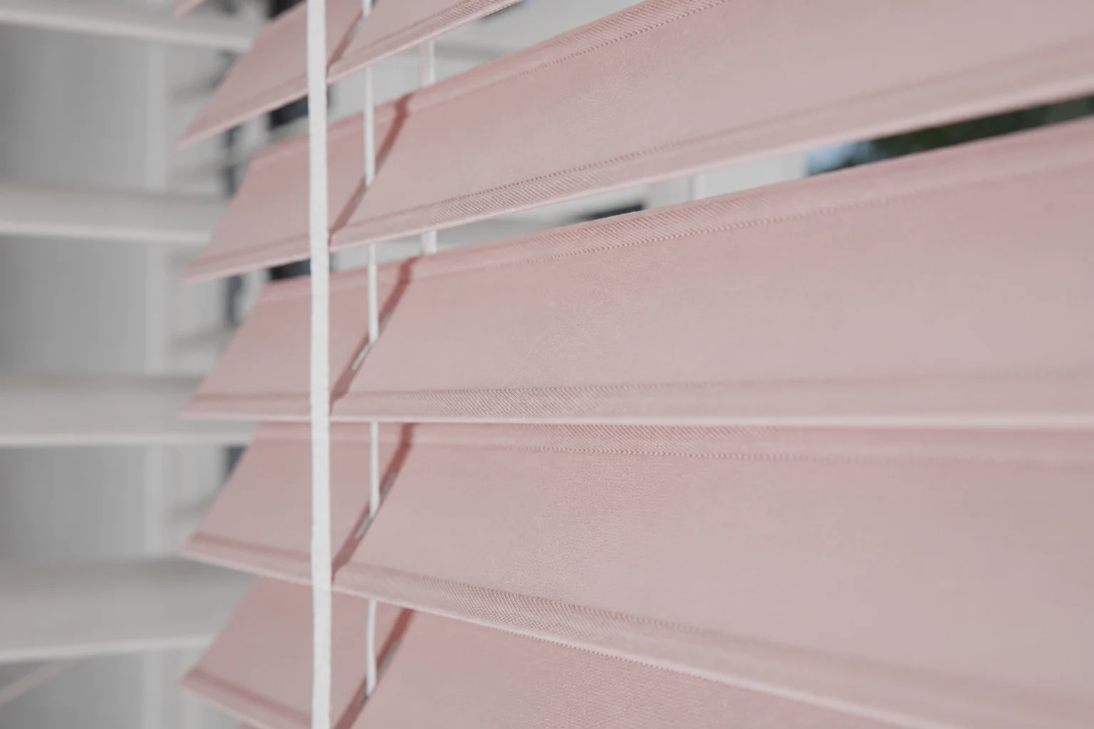 Close-up of pale pink horizontal Venetian slats, tilt cords and ladder strings.